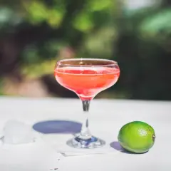 Orzeźwiający strawberry daiquiri w kieliszku, obok limonka i lód, na tle zieleni.