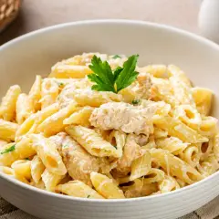 Penne z kurczakiem w kremowym sosie, idealne dania z makaronem na obiad. Udekorowane natką pietruszki.