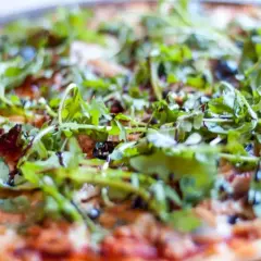 Pyszna pizza z tuńczykiem, rukolą i oliwkami, polana sosem balsamicznym.