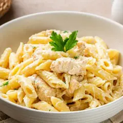Penne z kremowym sosem i kawałkami kurczaka, udekorowane natką pietruszki. Idealne na szybki obiad.