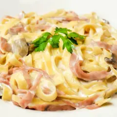 Tagliatelle z szynką i pieczarkami w kremowym sosie, z dodatkiem mozzarelli i natki pietruszki.