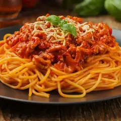 Pyszne spaghetti z mięsem mielonym w sosie pomidorowym, posypane serem i udekorowane bazylią. Idealny prosty przepis na obiad.
