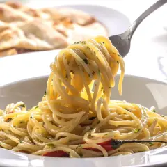 Widok z bliska na talerz pysznego, smażonego makaronu spaghetti z ziołami i kawałkami papryczki chili. Na drugim planie widać pieczywo.