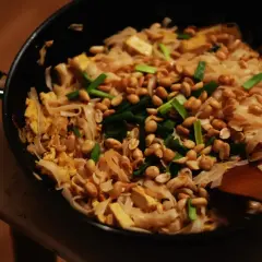 Gorący, gotowy do podania sos pad thai z makaronem ryżowym, tofu, orzeszkami ziemnymi i szczypiorkiem na patelni.