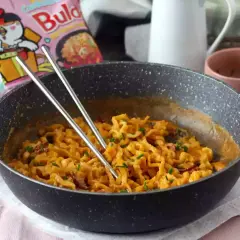 Pikantny buldak carbonara w patelni, gotowy do jedzenia. Obok paczka z tym daniem.