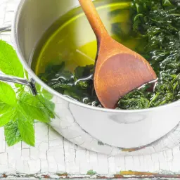 Gotowy syrop z mięty przepis: świeże liście mięty w garnku z wodą i drewnianą łyżką.