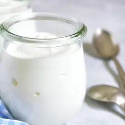 Dwa słoiczki pysznego, gładkiego jogurtu naturalnego, gotowe do spożycia. Obok leżą dwie łyżeczki.