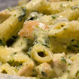 Penne z kurczakiem i zielonymi kawałkami szpinaku w kremowym sosie, posypane parmezanem. Pyszne danie z makaronem z kurczakiem i szpinakiem mrożonym.