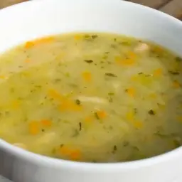 Zupa ogórkowa przepis babci. Aromatyczna, domowa zupa z kawałkami marchewki i ziół w białej miseczce na drewnianym tle.