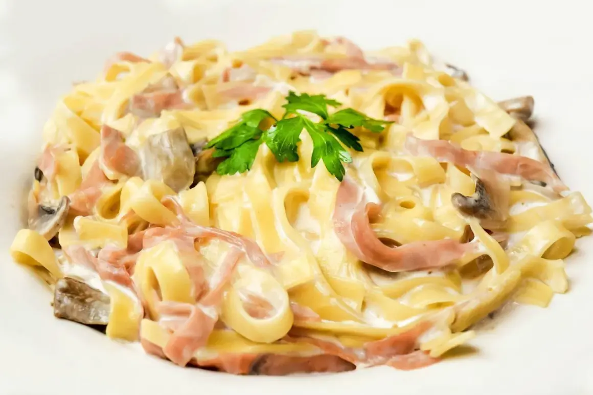 Tagliatelle z szynką i pieczarkami w kremowym sosie, z dodatkiem mozzarelli i natki pietruszki.