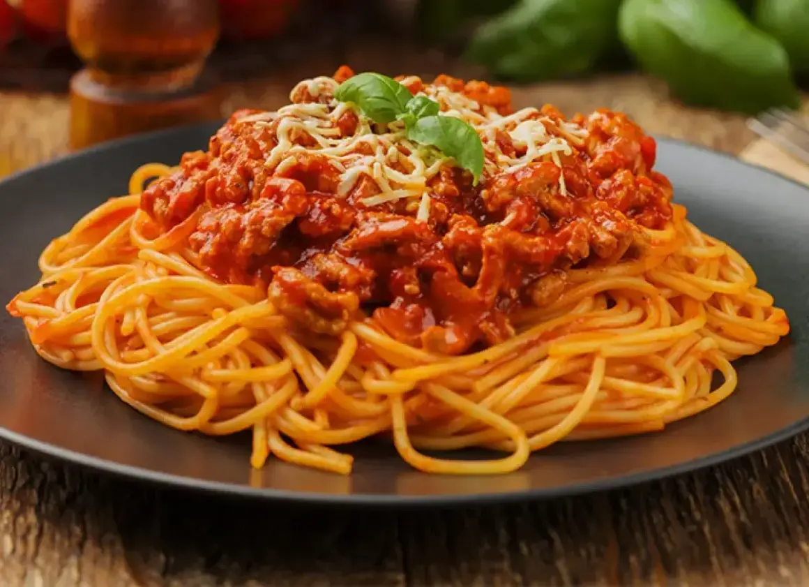 Pyszne spaghetti z mięsem mielonym w sosie pomidorowym, posypane serem i udekorowane bazylią. Idealny prosty przepis na obiad.