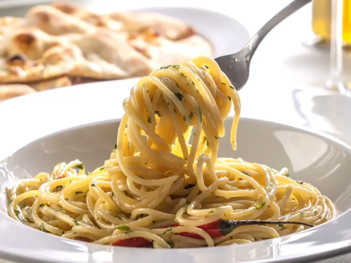 Widok z bliska na talerz pysznego, smażonego makaronu spaghetti z ziołami i kawałkami papryczki chili. Na drugim planie widać pieczywo.