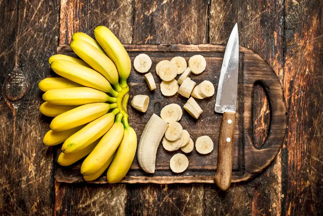 Pęczek bananów, pokrojone plasterki i nóż na desce. Zastanawiasz się, czy banany można trzymać w lodówce?