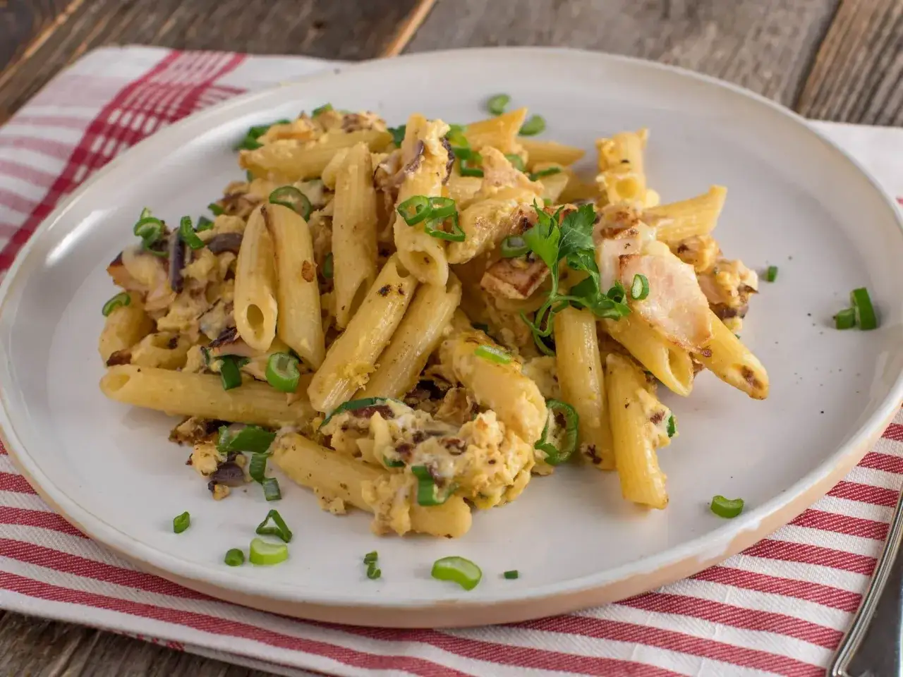 Pyszne dania z makaronem na obiad: penne z jajecznicą, boczkiem i szczypiorkiem, udekorowane natką pietruszki.