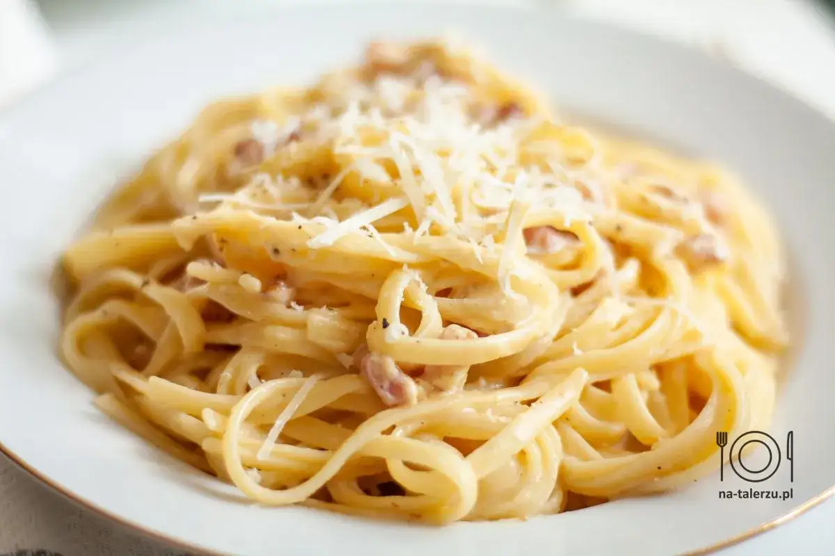 Kremowe spaghetti carbonara, przygotowane według oryginalnego przepisu ze śmietaną, posypane startym parmezanem i kawałkami guanciale.