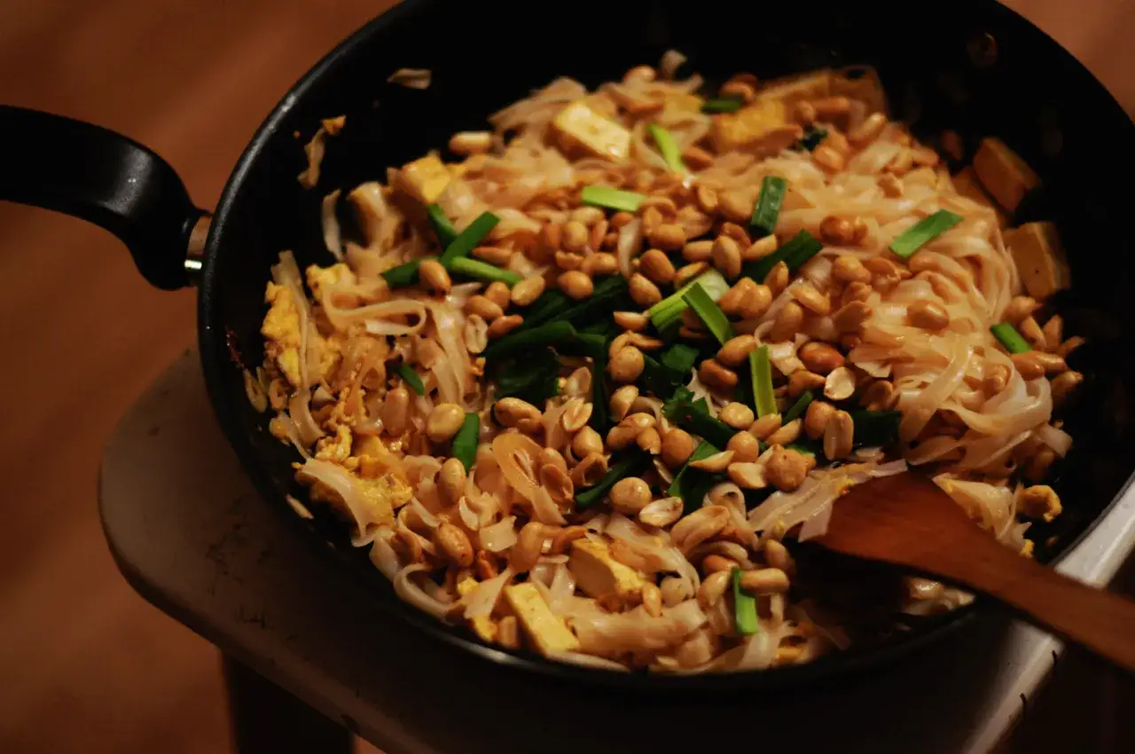 Pyszny sos pad thai z makaronem ryżowym, tofu, orzeszkami ziemnymi i szczypiorkiem w woku.