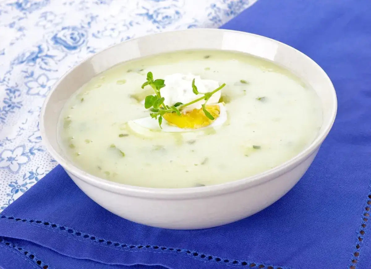 Kremowa zupa z sałaty z jajkiem i koperkiem, podana na niebieskim obrusie.