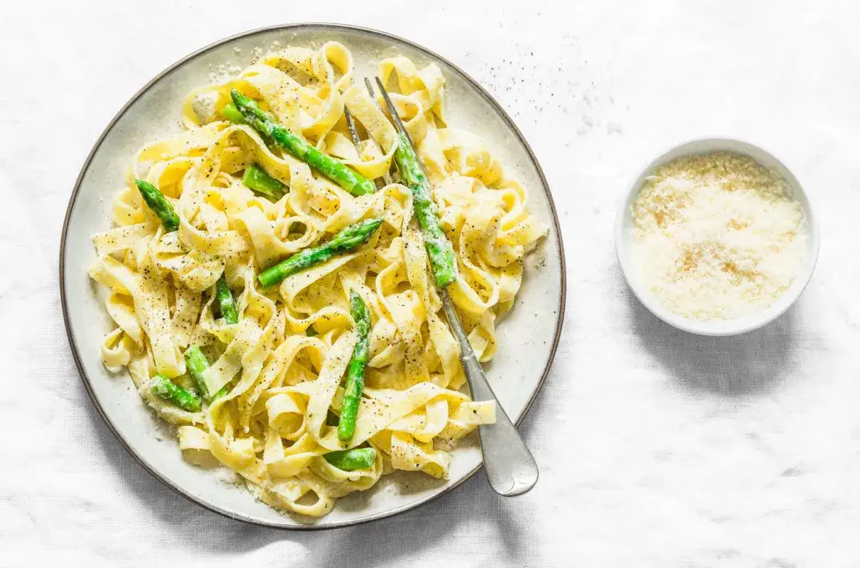 Tagliatelle ze szparagami w sosie śmietanowym, posypane parmezanem. Pyszne danie na talerzu.