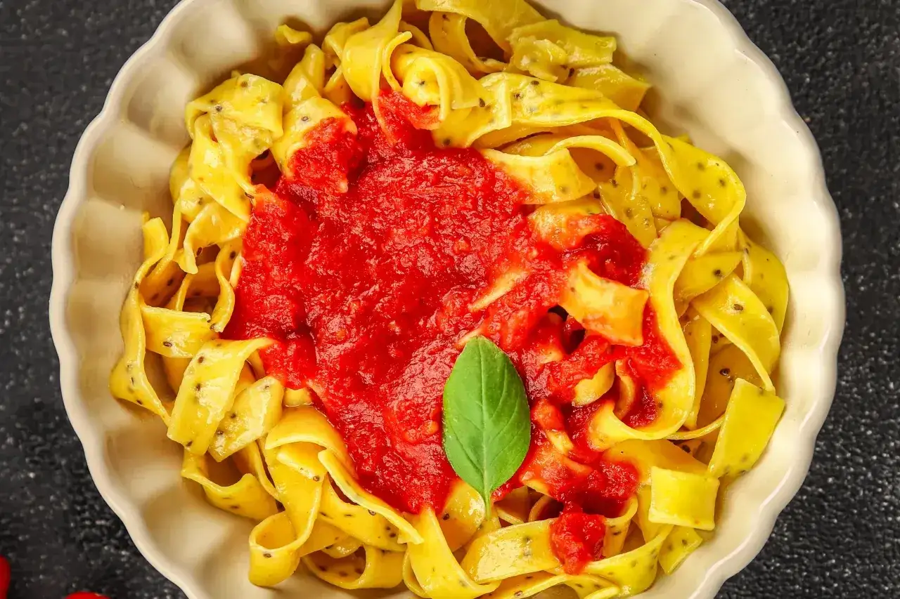 Pappardelle z domowym, aromatycznym sosem do makaronu pomidorowym, udekorowane listkiem bazylii.
