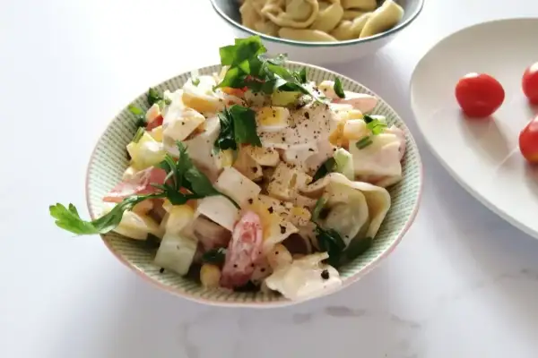 Pyszna sałatka z tortellini, jajka, kukurydzy i pomidorów, polana kremowym sosem. Idealna na szybki obiad lub kolację.